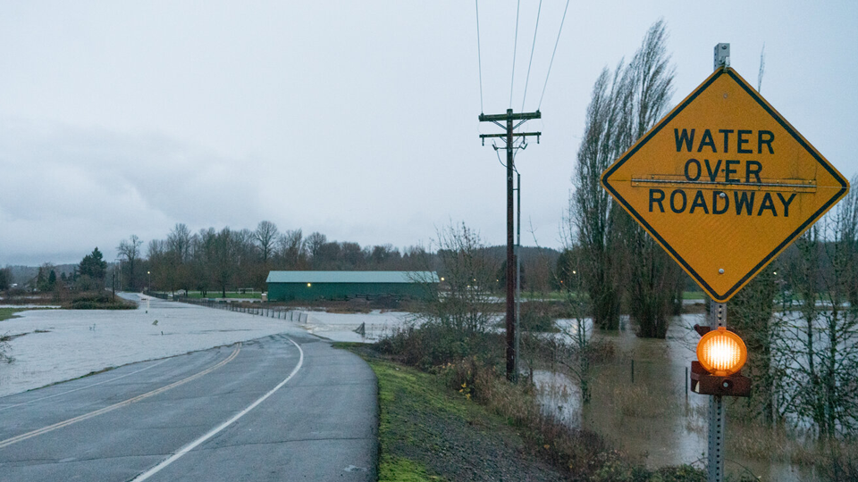 news-newsletter Sign that reads "water over roadway" along a flooded road